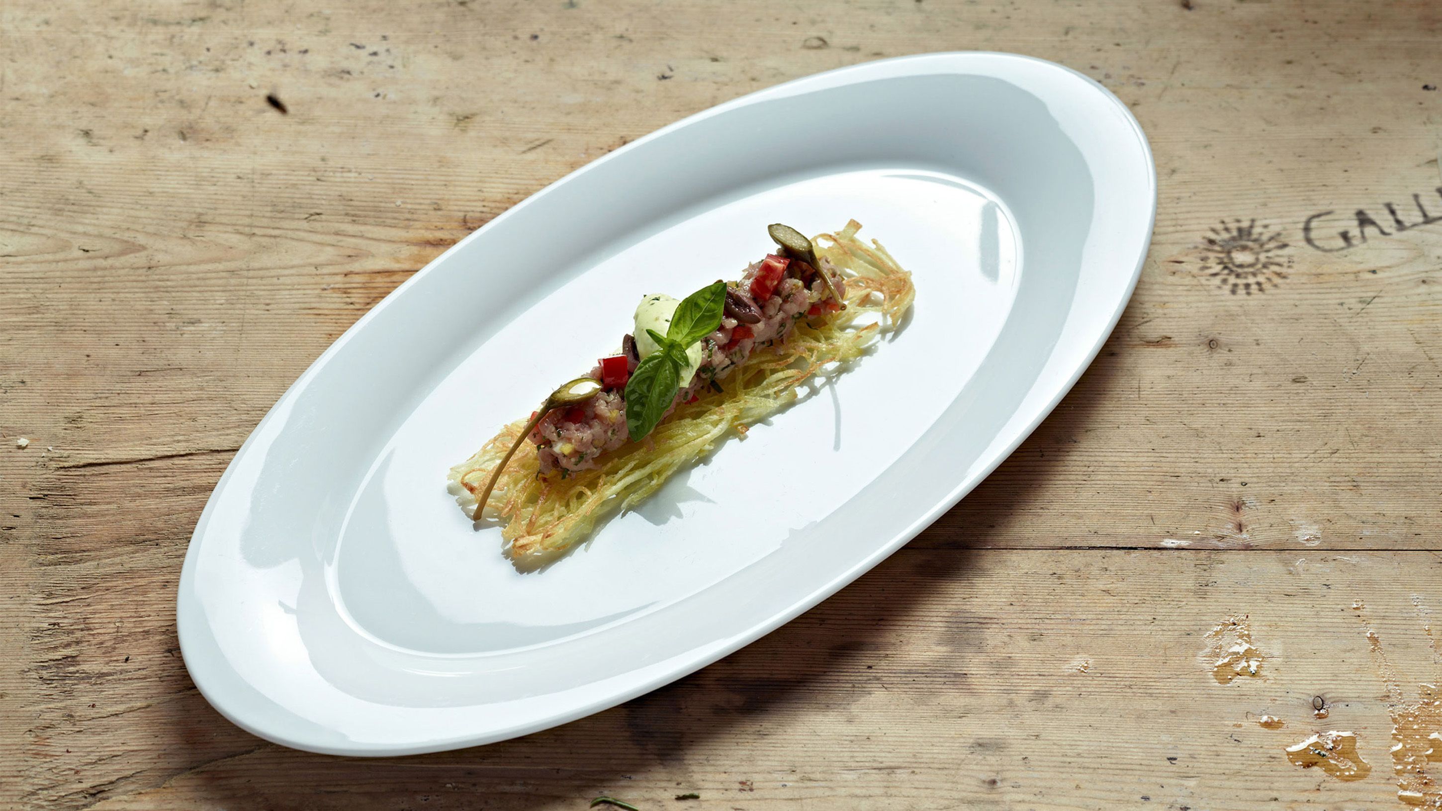 Un plato ovalado blanco con un recipiente sobre una mesa de madera.