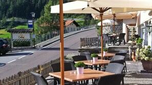 Un restaurante al aire libre con mesas y sillas, un letrero que dice 'Gallia Gasthof Restaurant Albergos', y una carretera con barandilla.