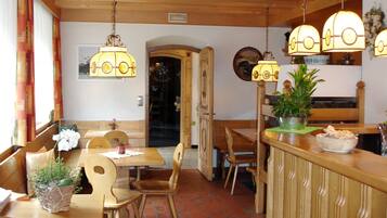 Interior de restaurante con mobiliario de madera, lámparas colgantes y plantas en macetas.