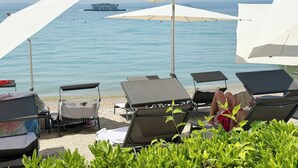 A beach with lounge chairs, umbrellas, and a boat in the water. - Hotel Sportsman (Bardolino)