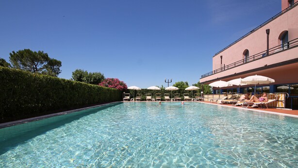 A clear swimming pool with lounge chairs and umbrellas, surrounded by a hedge and a building with balconies. - Hotel Sportsman (Bardolino)
