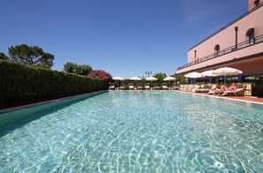 A clear swimming pool with lounge chairs and umbrellas, surrounded by a hedge and a building with balconies. - Hotel Sportsman (Bardolino)