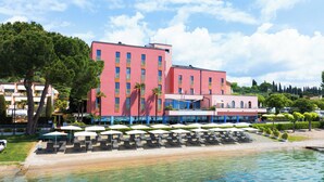 A hotel with a red facade, multiple balconies, and outdoor seating by the water. - Hotel Sportsman (Bardolino)