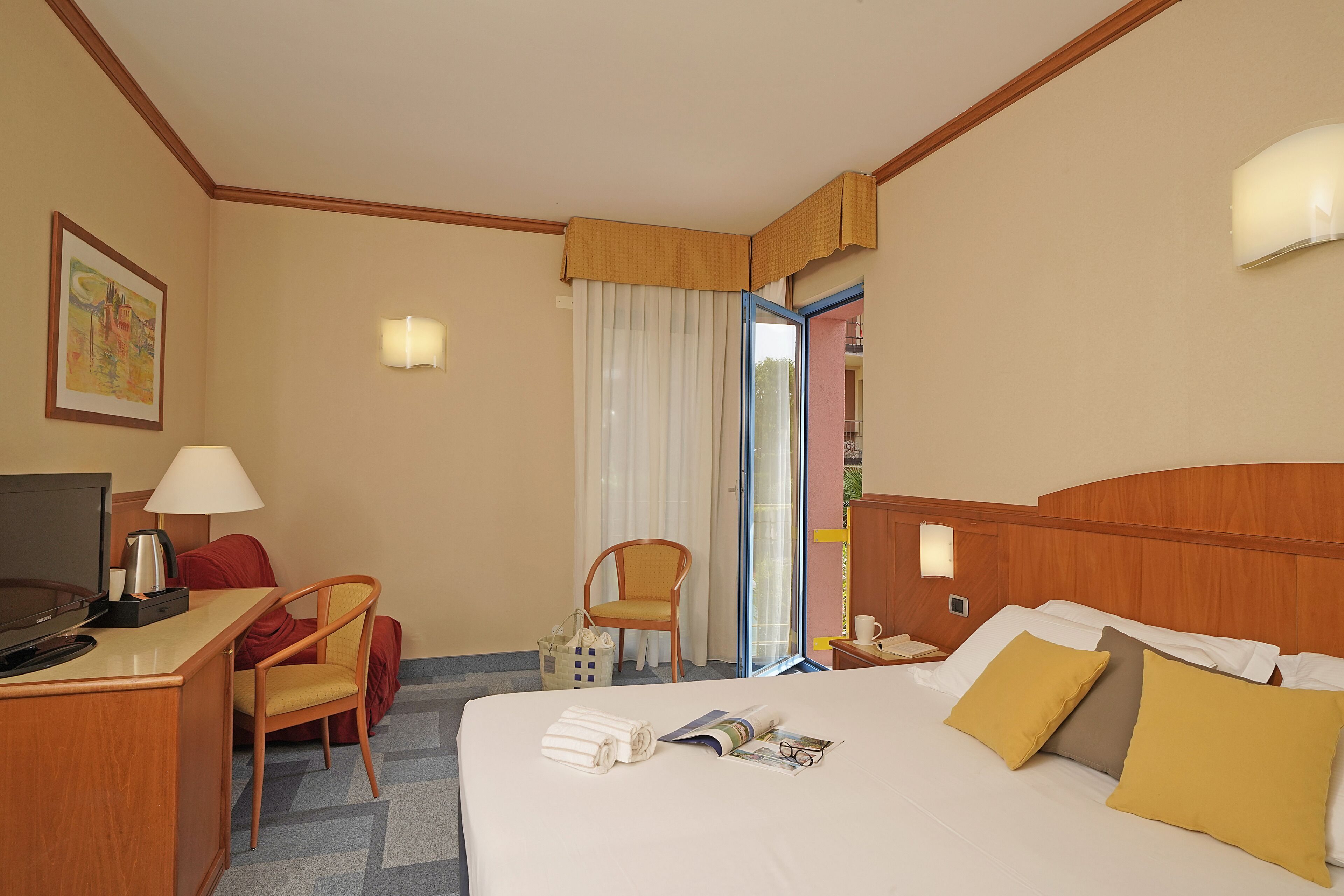 A hotel room with a bed, a desk with a TV, a chair, a lamp, and a window with curtains.