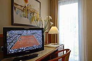 A television displaying a tennis match, a vase with white flowers, a lamp, and a framed artwork on the wall. - Hotel Sportsman (Bardolino)