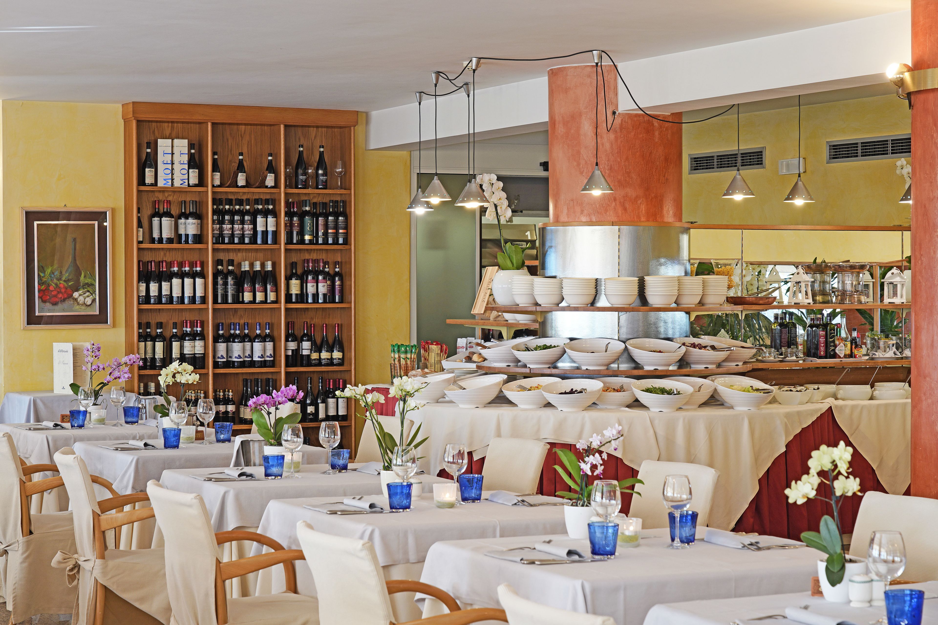 Un restaurante con varias mesas dispuestas para comer, una exhibición de vinos y licores, y una variedad de platos en la barra.