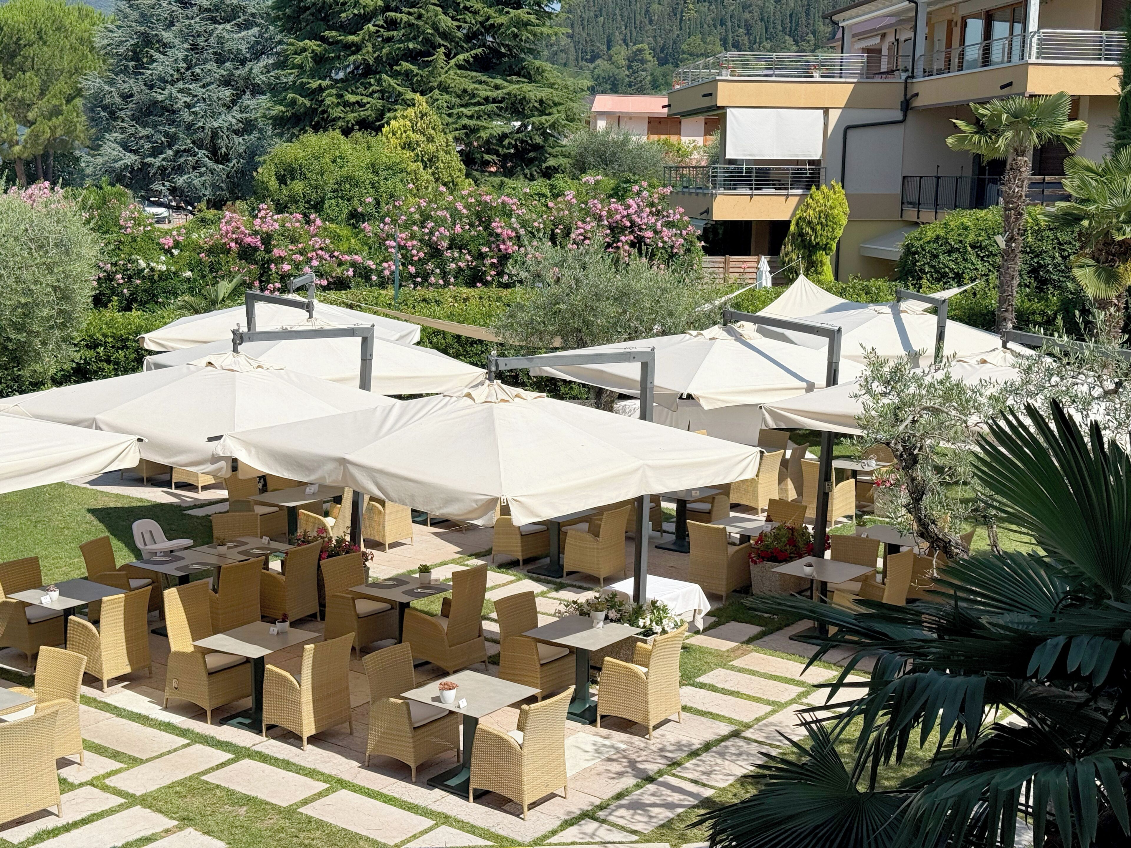 Outdoor seating with umbrellas, wicker furniture, and a landscaped garden with trees and shrubs.