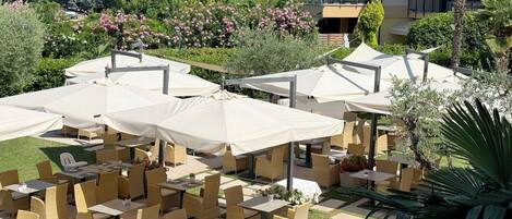 Outdoor seating with umbrellas, wicker furniture, and a landscaped garden with trees and shrubs.