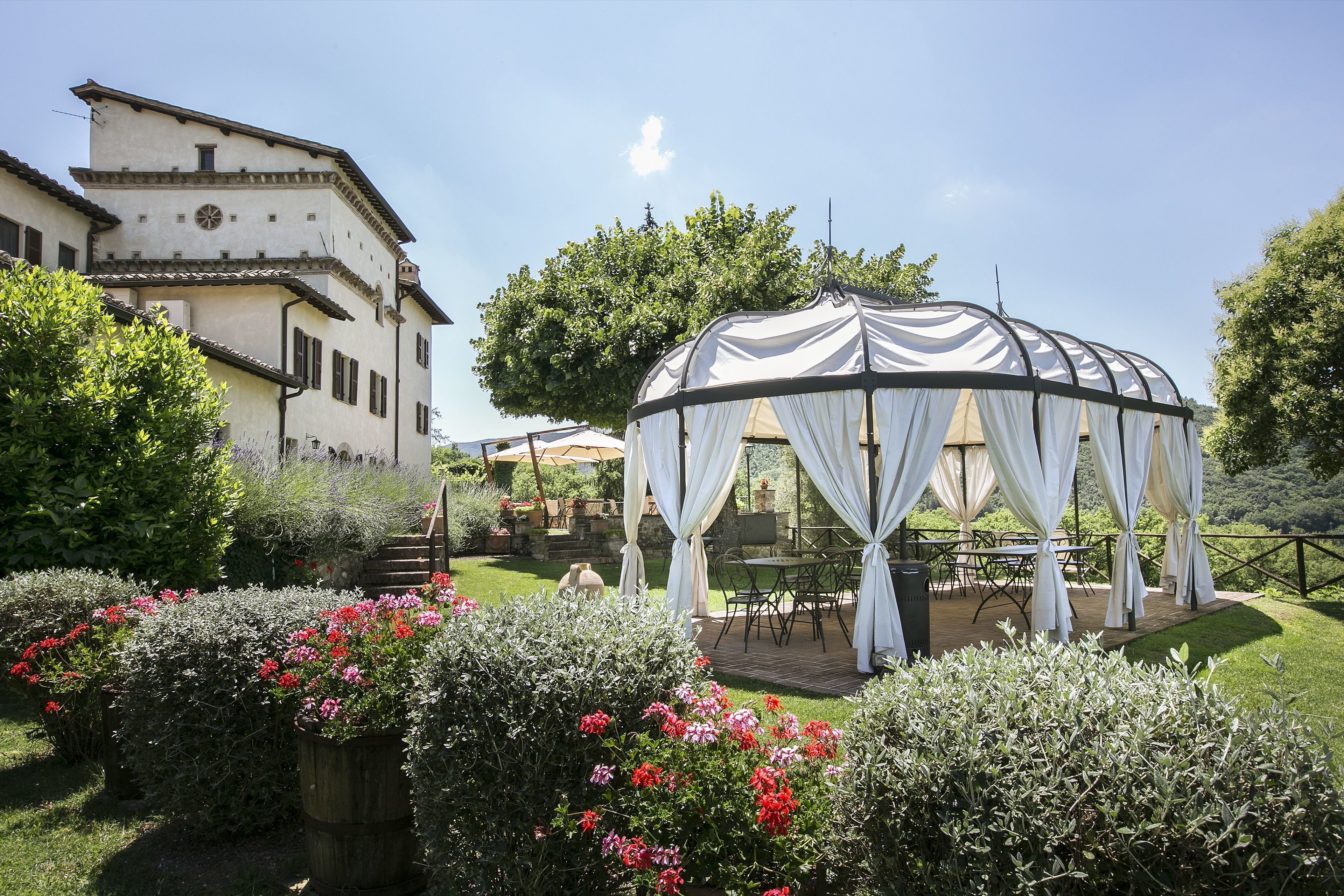 A gazebo with white drapes, a patio area with tables and chairs, and a building with a clock and windows.
