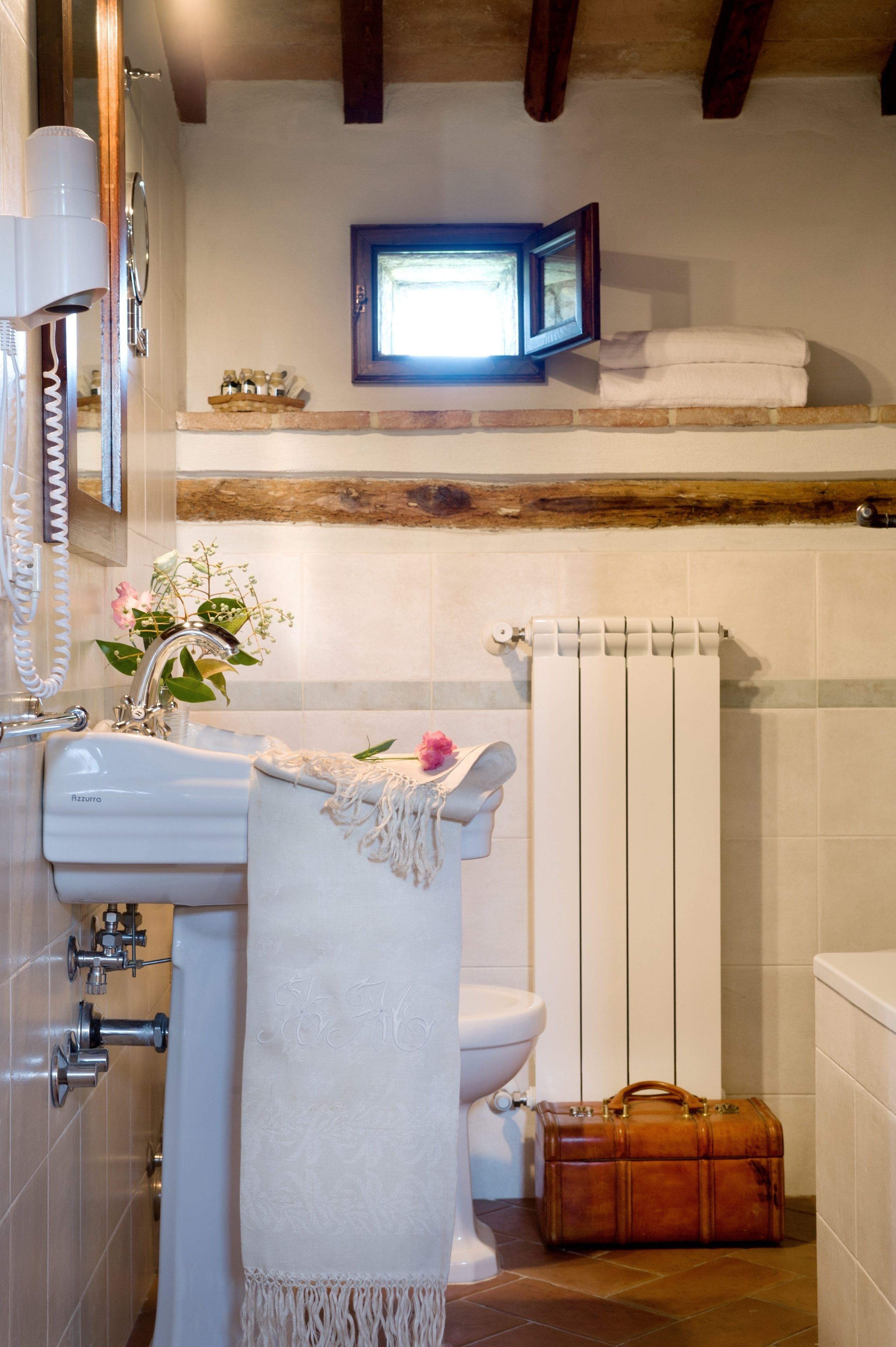 A bathroom with a white sink, a toilet, a radiator, and a wooden bench.