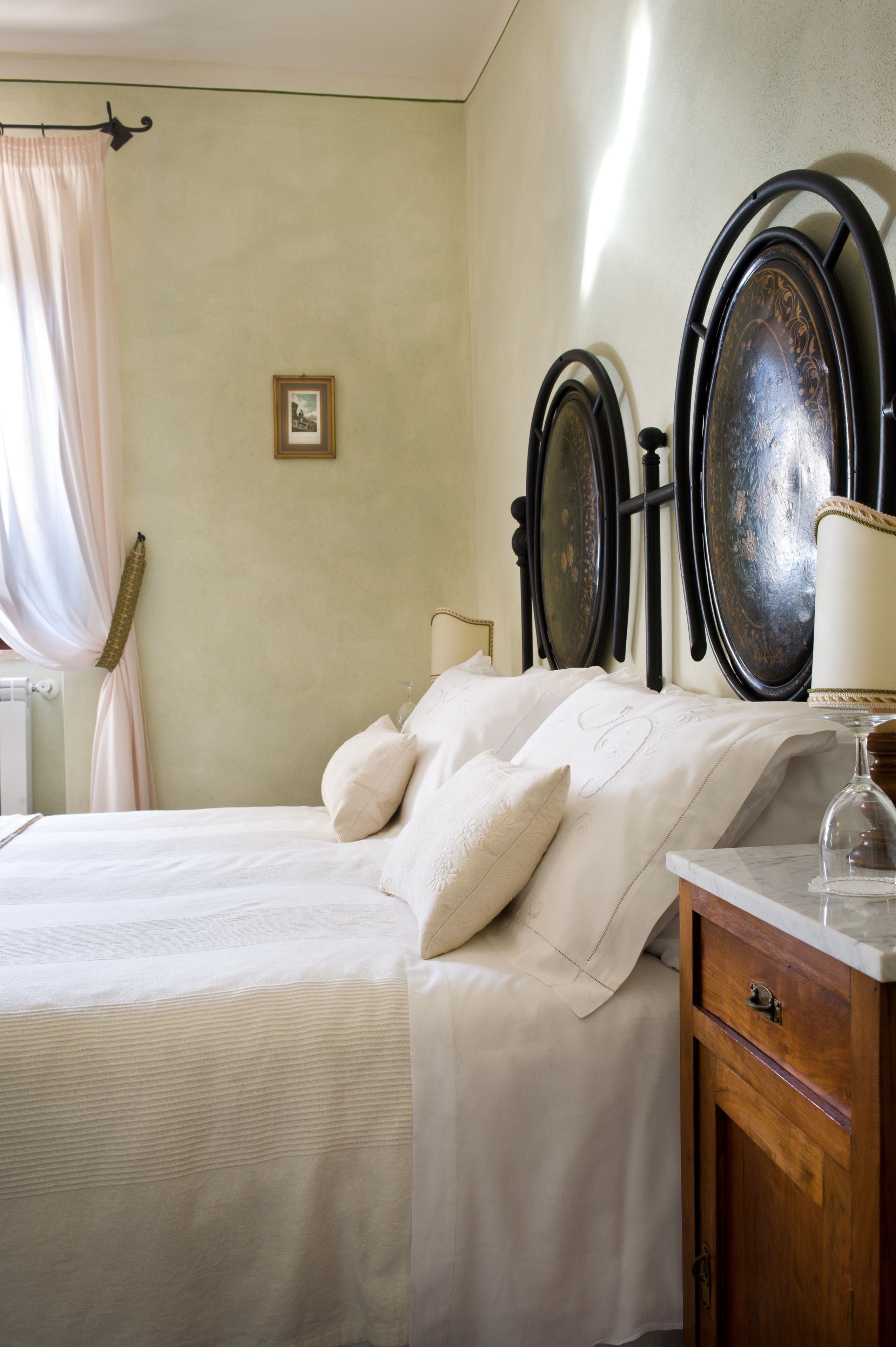 A neatly made bed with a headboard, a bedside table with a lamp, and a wall-mounted mirror.