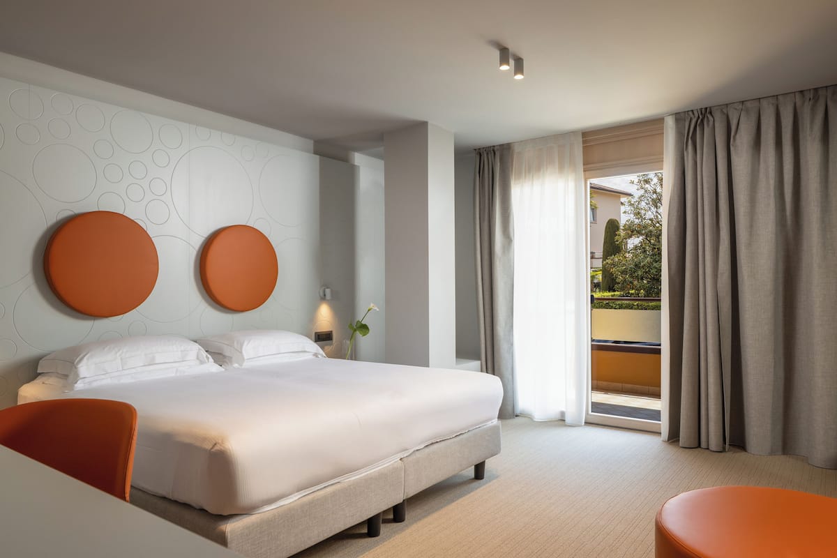 Una habitación de hotel moderna con una cama grande, zona de estar y balcón con cortinas.