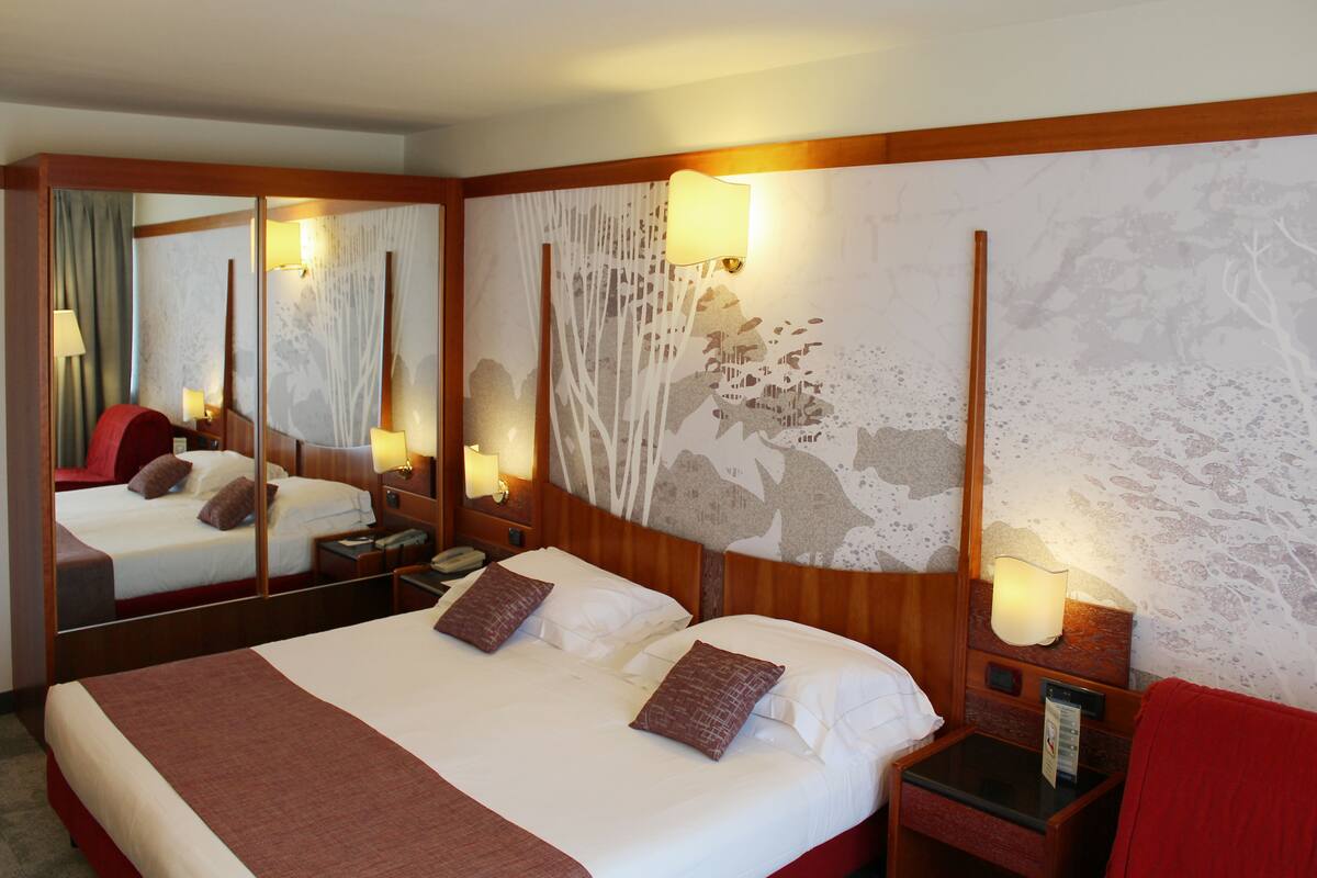 Una habitación de hotel con una cama grande, una mesita de noche con lámpara, un espejo y una pared con diseño decorativo.