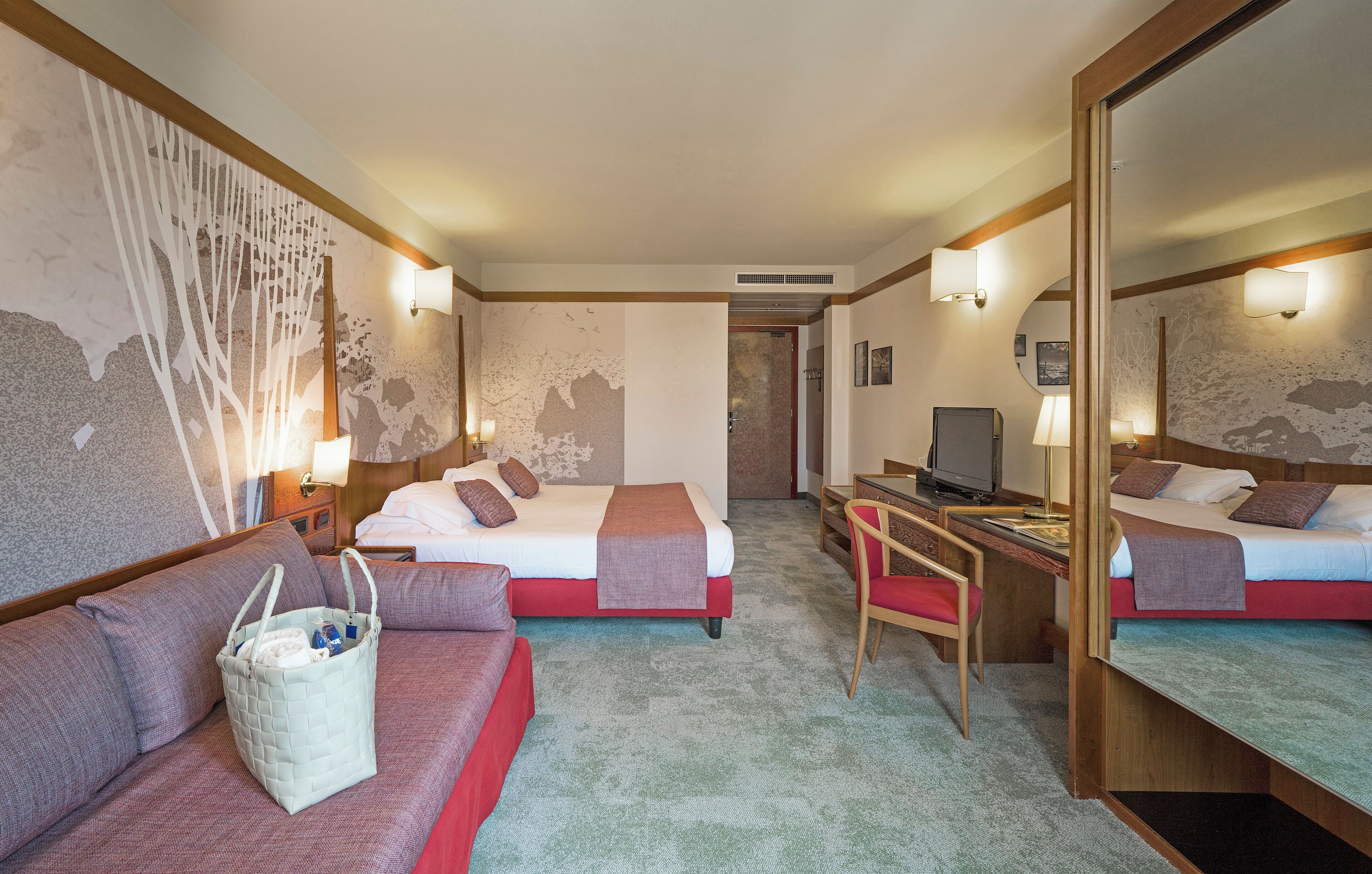 A hotel room with two beds, a desk, a chair, a sofa, a large mirror, and a wall with a unique textured design.