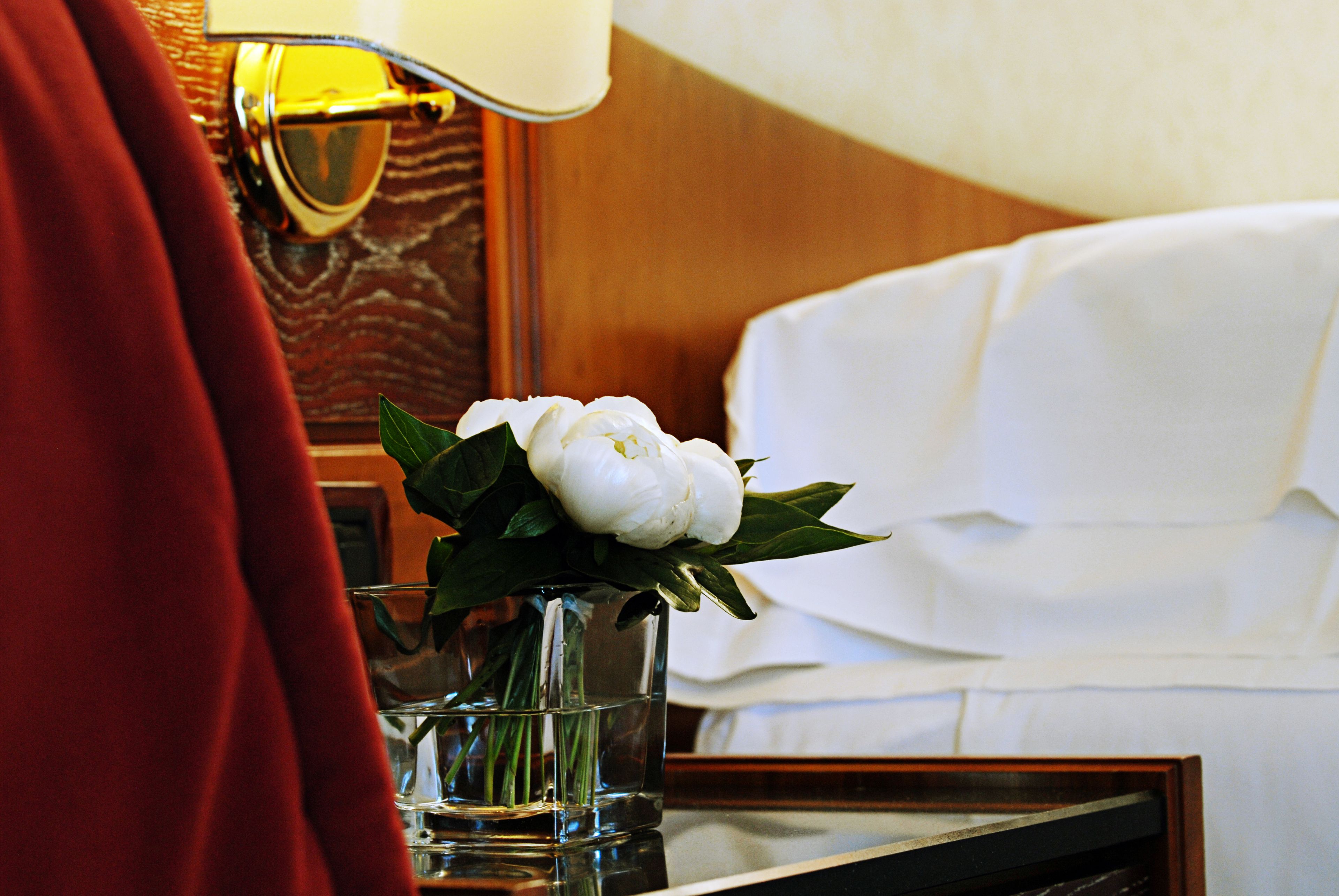 A hotel room with a bed, a bedside table with a vase of flowers, and a lamp.