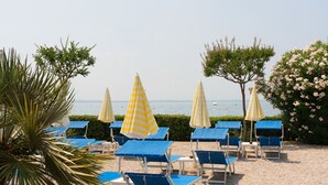 Un área de descanso en la playa con sillones azules y sombrillas a rayas amarillas, con vista al mar.
