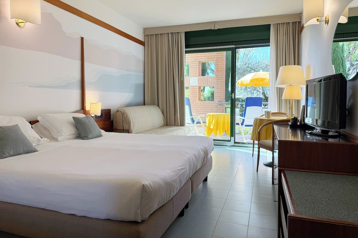 Habitación de hotel con una cama grande, televisión y balcón con mobiliario exterior.
