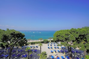Une vue sur la plage, avec des rangées de chaises longues et de parasols, un ciel dégagé et la mer en arrière-plan.