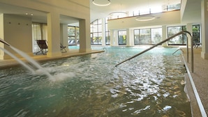Una piscina interior con agua cristalina, iluminación moderna y grandes ventanales.