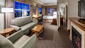 A hotel room with a sofa, armchair, small table, and a fireplace. - Heritage Inn & Suites (Brooks)