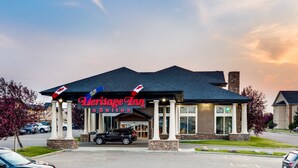 A Heritage Inn Suites building with a dark roof, white columns, and a sign displaying the name. - Heritage Inn & Suites (Brooks)
