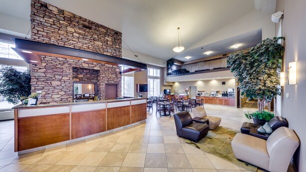 A spacious lobby with a stone fireplace, a reception desk, comfortable seating, and a balcony with a view. - Heritage Inn & Suites (Brooks)
