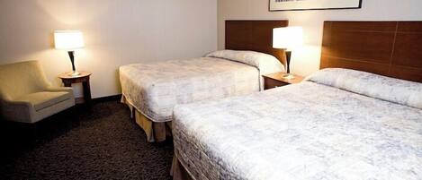 A hotel room with two beds, a chair, and a small table with lamps.