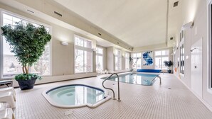 An indoor swimming pool with tiled flooring, a seating area, and a large potted plant. - Heritage Inn & Suites (Brooks)
