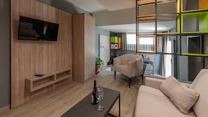 A modern living room with a flat-screen TV, a sofa, a coffee table with a bottle and glass, and a dining area in the background. - NataLis Apartamentos (Pajara)