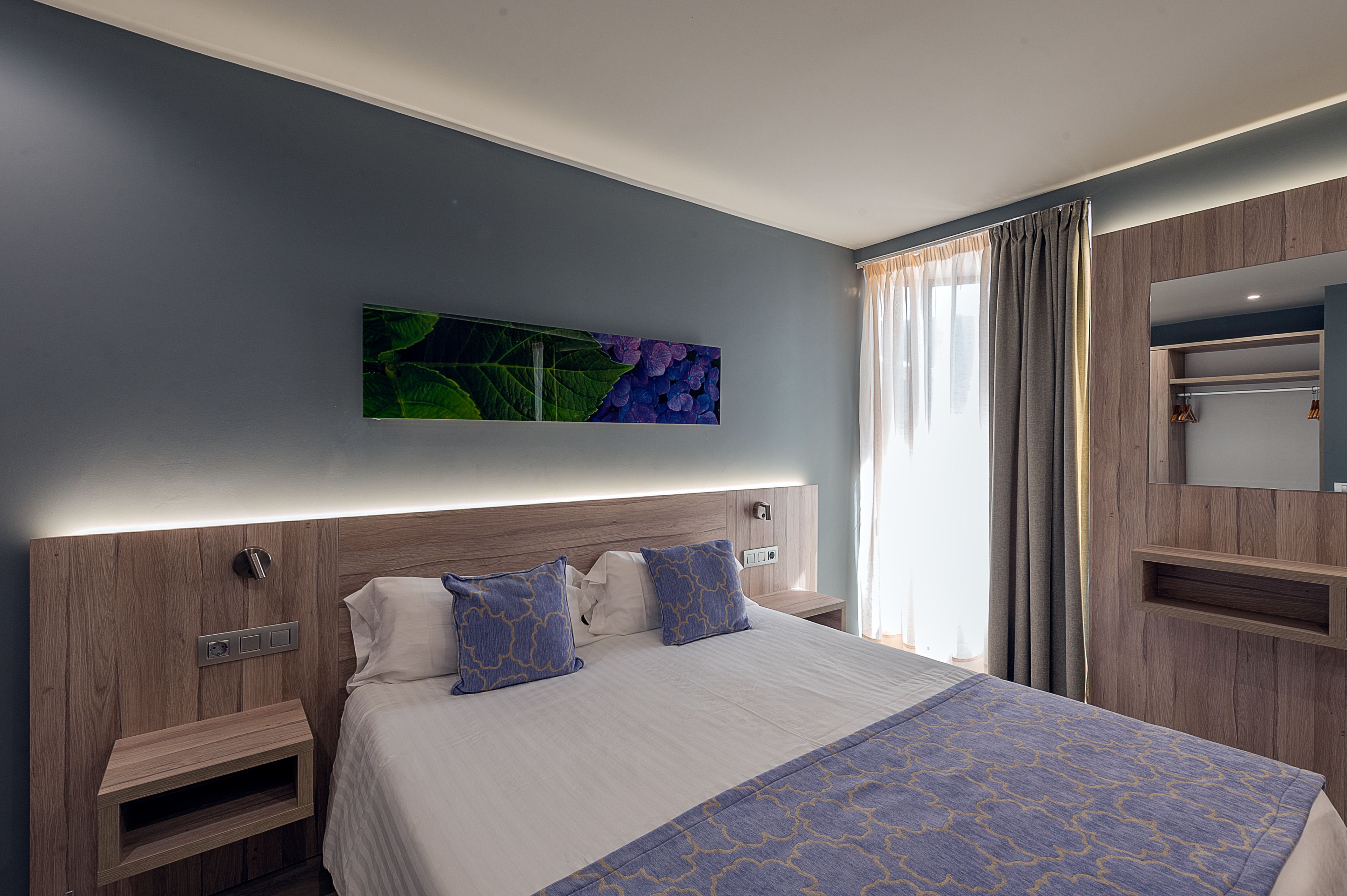 A modern hotel room with a large bed, a nightstand, a wall-mounted TV, and a wardrobe.