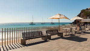 A seaside patio with benches, tables, and umbrellas overlooking the ocean. - NataLis Apartamentos (Pajara)