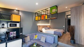 Una habitación de hotel compacta con kitchenette, un sofá, una cama y una lámpara de techo original.