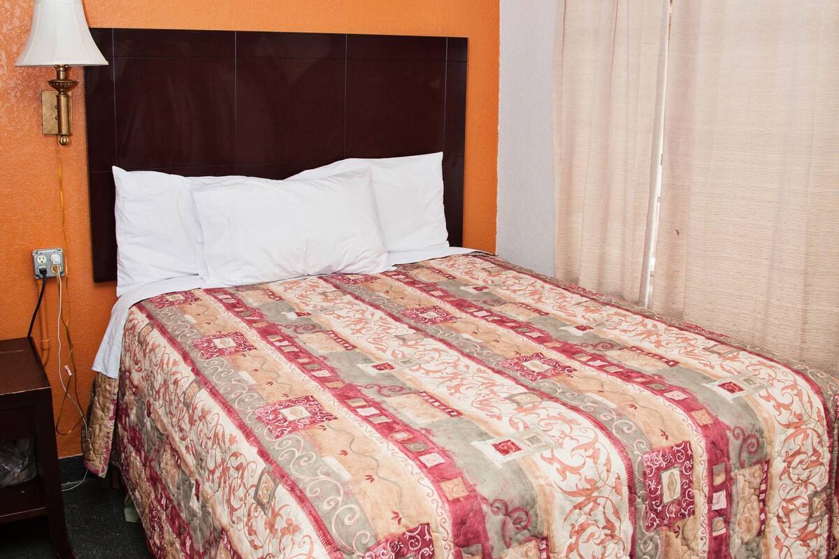A bed with a patterned bedspread, a bedside lamp, and a nightstand with a power outlet.