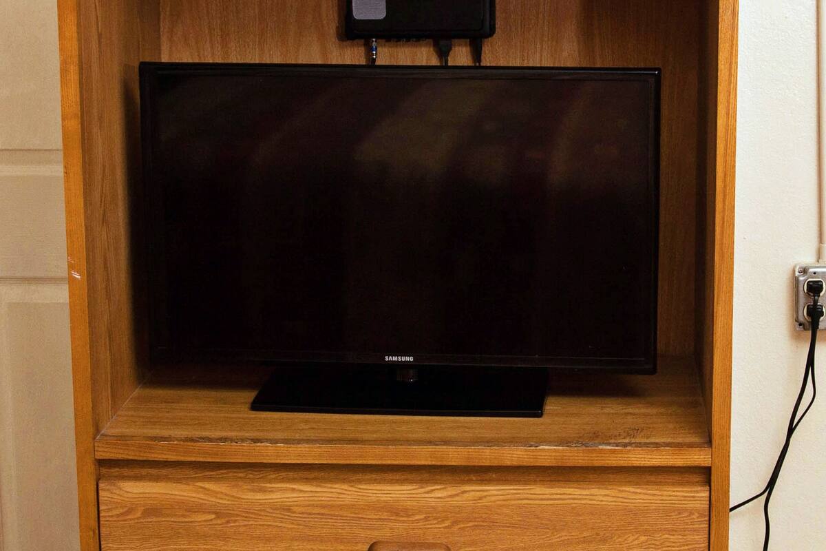 A wooden entertainment center with a flat-screen TV, a USB charging port, and a power outlet on the wall.