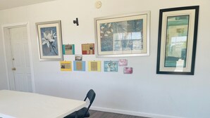 Une pièce avec une table blanche, des chaises noires et un mur décoré de tableaux encadrés et de petites affiches.