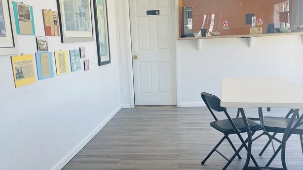 Une pièce avec une porte blanche, des tableaux encadrés accrochés au mur, une table avec des chaises et un plancher en bois.