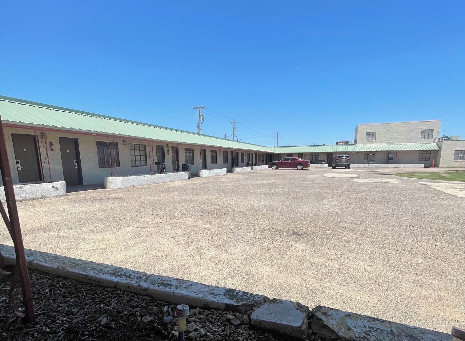 Un motel con estacionamiento de grava y varias habitaciones con techos verdes.