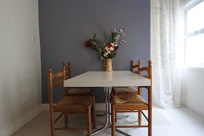 A dining table with four wooden chairs, a vase with flowers, and a window with curtains. - Black Rooster Guesthouse (Prince Rupert)