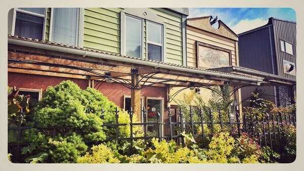 A row of historic buildings with a covered walkway, a sign for 'Black Rooster Inn', and lush greenery in front. - Black Rooster Guesthouse (Prince Rupert)