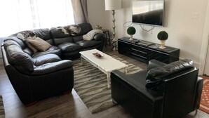 A modern living room with a leather sofa, a coffee table, a TV, and a side table with decorative items. - Black Rooster Guesthouse (Prince Rupert)