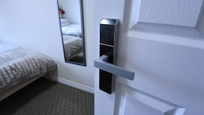 Habitación de hotel con cama, mesita de noche, espejo y puerta con pomo moderno.