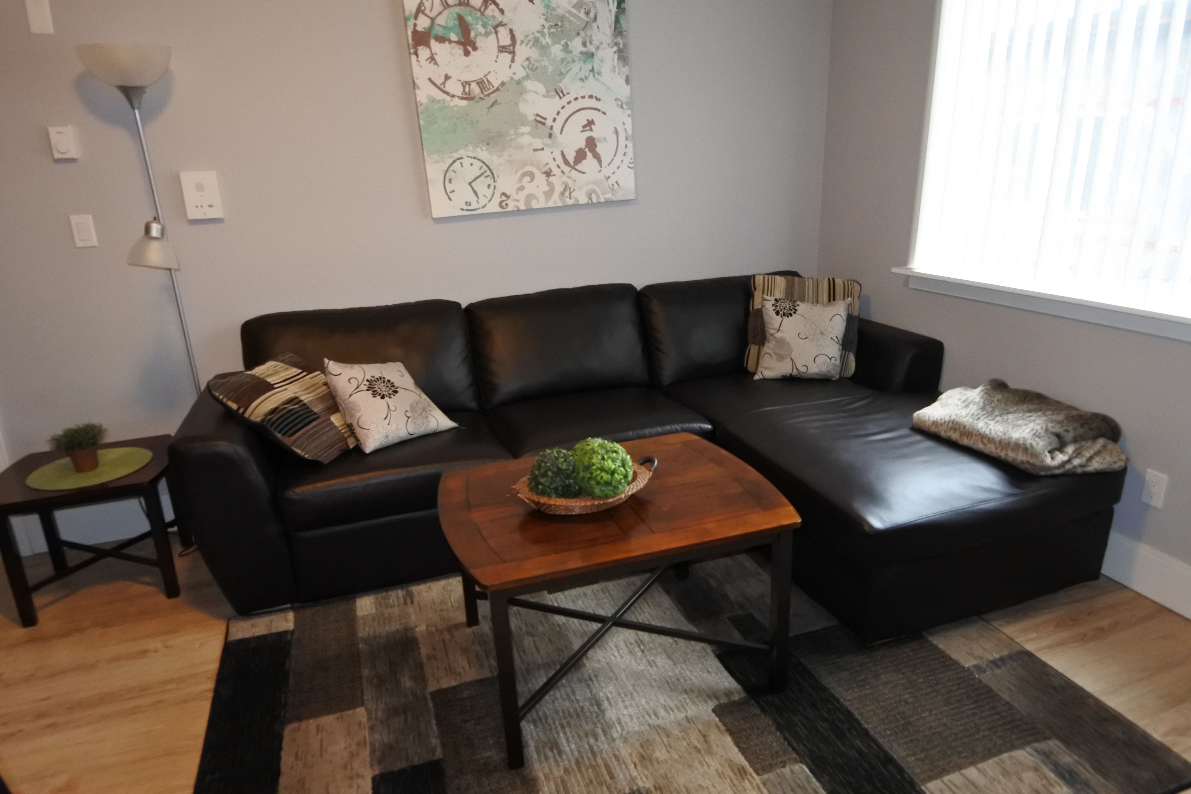 A modern living room with a black leather sofa, a wooden coffee table, and a decorative wall clock.