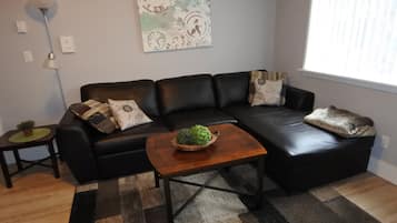 A modern living room with a black leather sofa, a wooden coffee table, and a decorative wall clock.