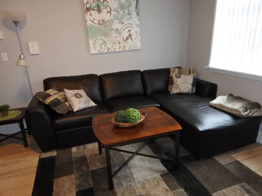 A modern living room with a black leather sofa, a wooden coffee table, and a decorative wall clock.