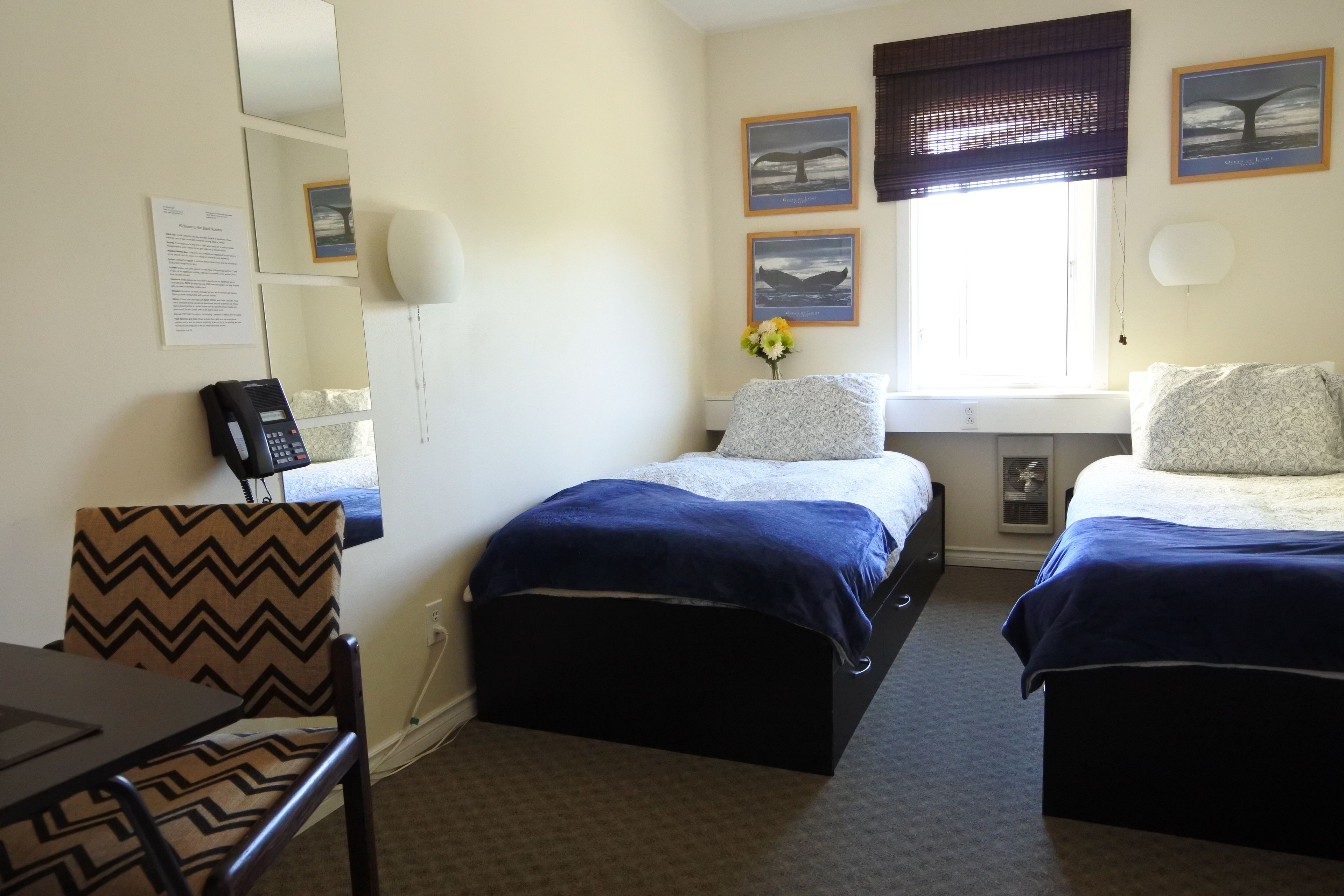 A hotel room with two beds, a desk, a chair, a phone, and artwork on the walls.