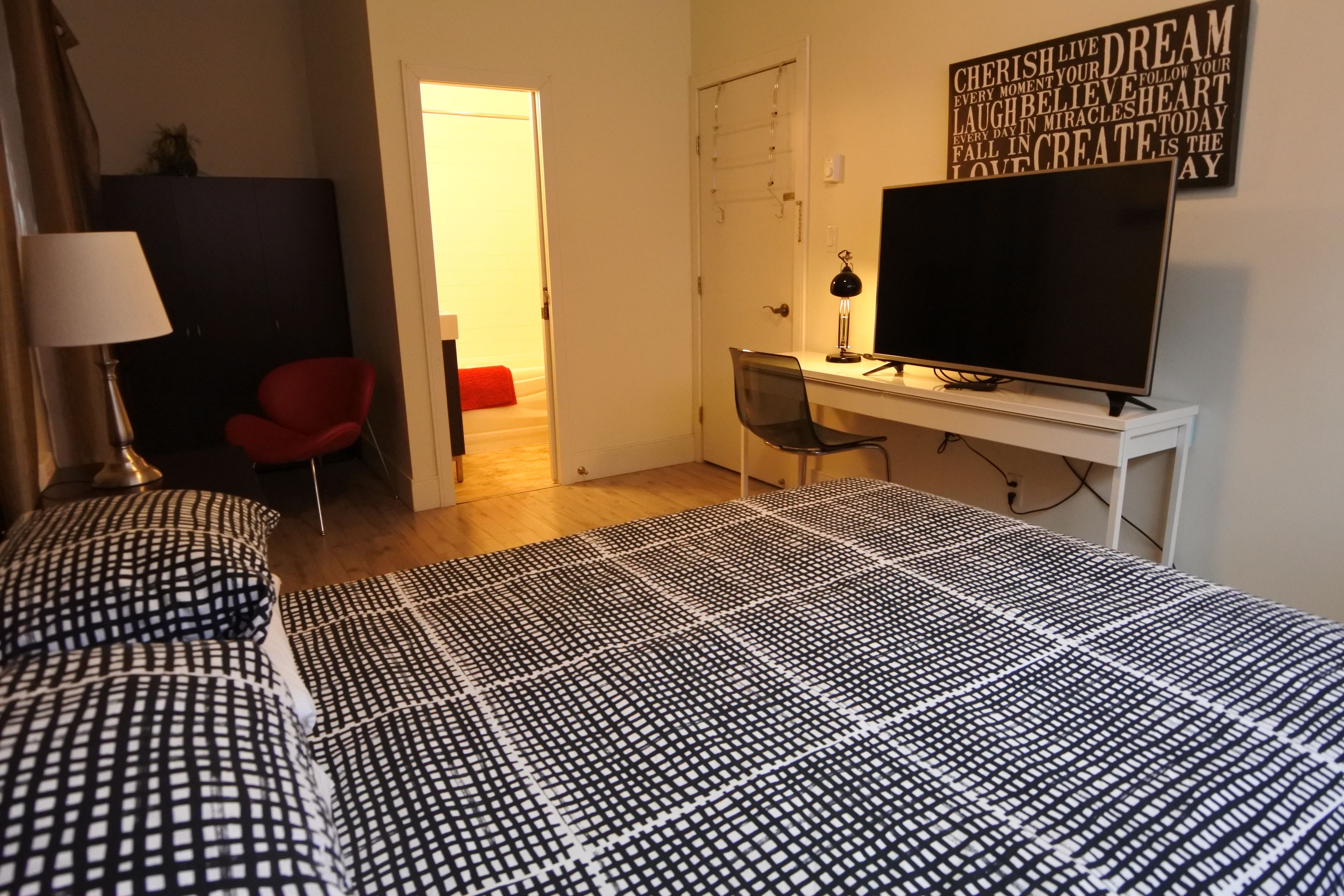 A bedroom with a bed, a desk, a chair, a TV, and a motivational quote on the wall.