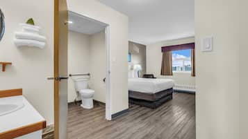 A hotel room with a wooden floor, a bed, a bedside table, a lamp, and a view of the city through the window.