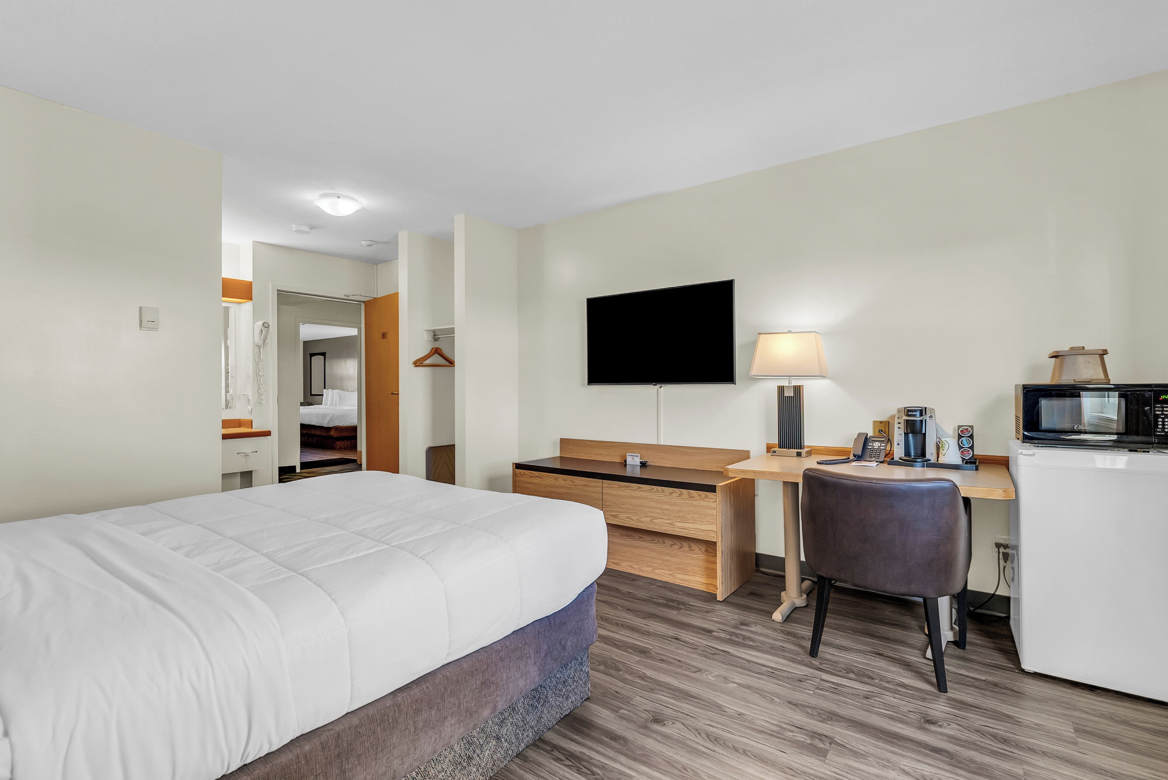 Habitación de hotel con cama, escritorio, silla, televisor, lámpara y microondas.