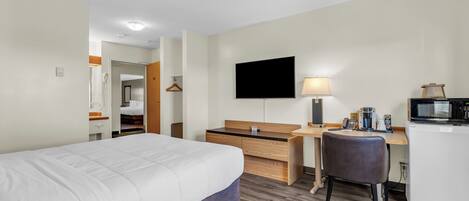 Habitación de hotel con cama, escritorio, silla, televisor, lámpara y microondas.