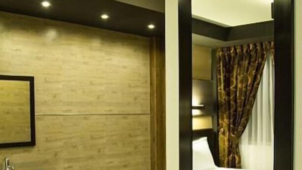 Quarto de hotel moderno com piso de madeira, um espelho grande, uma cama com roupa de cama branca, mesa de cabeceira e banheiro com pia e banheira.